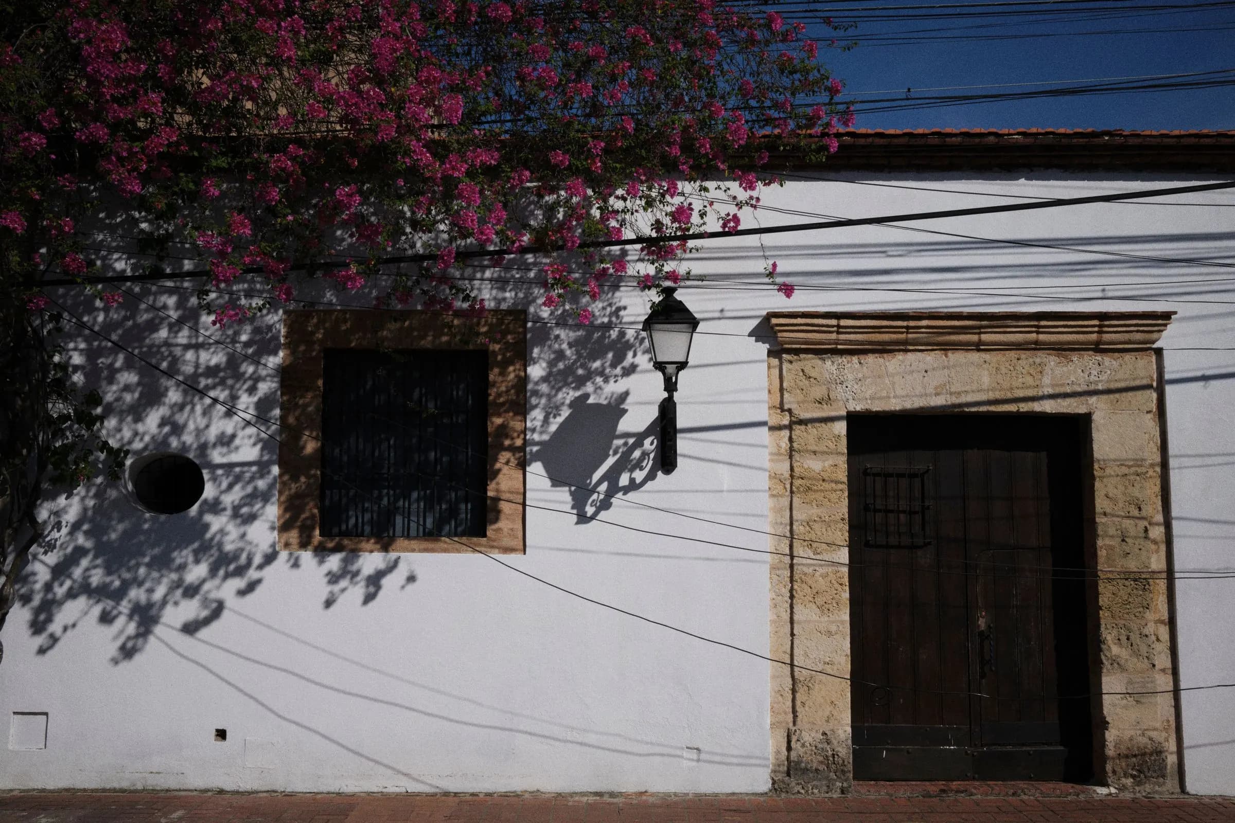 Fachada colonial blanca con puerta de piedra y buganvilla.